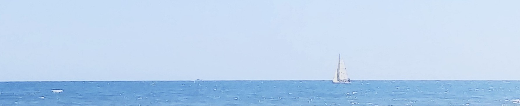 Mer calme avec voilier et cargo à l’horizon